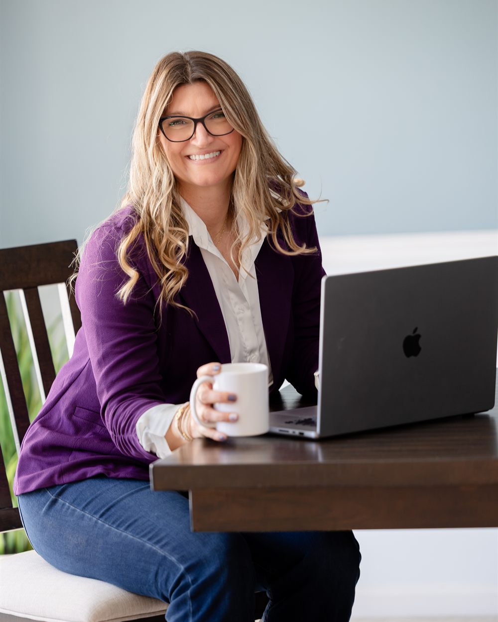 Alison smiling at her desk with a coffee mug and laptop